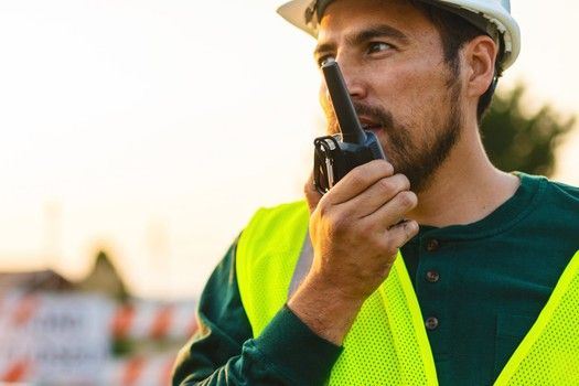 Ein Arbeiter spricht in ein Walkie-Talkie vor einer Stra&szlig;enabsperrung
